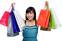 Young woman wearing blue dress and holding colorful shopping bags up in air - Asia Images Group