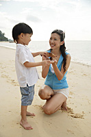 Mother and son on beach, boy holding wooden airplane - Asia Images Group