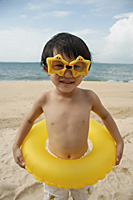 Young boy on beach wearing yellow star goggles and holding yellow float around waist - Asia Images Group