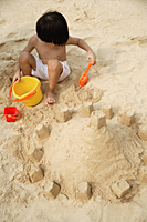 Young boy on beach building sand castle - Asia Images Group