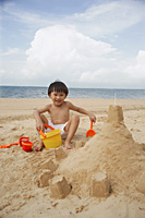 Young boy on beach building sand castle, smiling - Asia Images Group