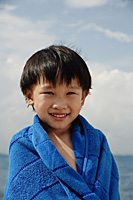 Young boy on beach wrapped in blue towel - Asia Images Group