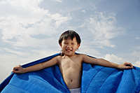 Young boy on beach with blue towel flying behind him - Asia Images Group