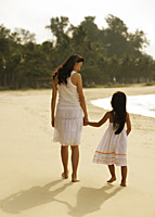Mother and daughter walking hand and hand on beach, wearing white dresses - Asia Images Group