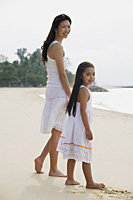 Mother and daughter standing on beach, wearing white dresses - Asia Images Group