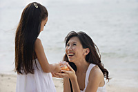 Mother and daughter on beach, daughter handing conk shell to mother, smiling - Asia Images Group