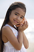 Young girl on beach holding conk shell to her ear, smiling - Asia Images Group