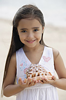 Young girl on beach holding giant conk shell in her hands, smiling - Asia Images Group