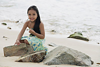Young girl sitting on beach by rocks - Asia Images Group