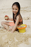 Young girl building sand castle on beach, smiling - Asia Images Group