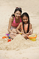 Mother and daughter sitting in sand on beach, building sand castle - Asia Images Group