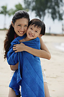 Mother hugging son on beach, son wrapped in blue towel - Asia Images Group