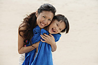 Mother hugging son on beach, son wrapped in blue towel, smiling - Asia Images Group