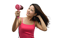 Young woman blow drying hair and looking at camera - Asia Images Group