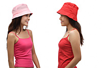 Two young women wearing pink and red hats, looking at each other - Asia Images Group