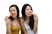 Two young women biting into Popsicle, looking at camera - Asia Images Group