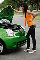 A young woman looks under the hood of a car - Asia Images Group