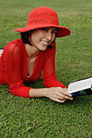 A woman reads while lying on grass - Asia Images Group