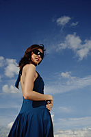 A young woman with sunglasses stands with the sky in the background - Asia Images Group