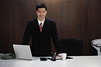 A businessman stands behind his desk - Asia Images Group