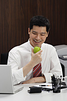 A man eats an apple at his desk - Asia Images Group