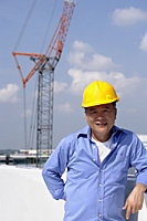 A man with a yellow helmet smiles at the camera as he works - Asia Images Group