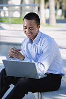 A man smiles as he uses his laptop outdoors - Asia Images Group