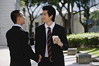 Two men wearing suits greet each other and shake hands in the park - Asia Images Group