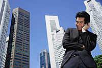 A man talks on his cellphone with skyscrapers in the background - Asia Images Group