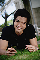 A man looks at the camera as he listens to music on a mp3 player in the park - Asia Images Group