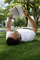 A man lies down and reads in the park - Asia Images Group