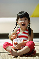 A small girl plays with a doll as she looks at the camera - Asia Images Group