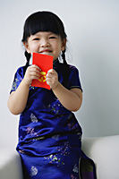 A small girl holds a red packet as she looks at the camera - Asia Images Group