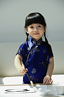 A small girl in blue silk cheongsam writing Chinese calligraphy - Asia Images Group