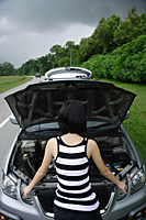 A woman checks under the hood of her car - Asia Images Group