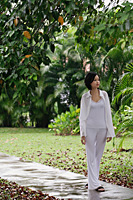 A woman strolls down a path in a garden - Asia Images Group