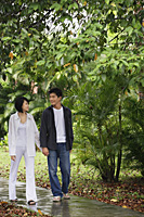 A young couple hold hands and stroll down a garden path together - Asia Images Group