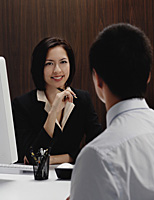 A woman sits at her desk while she talks with a man - Asia Images Group