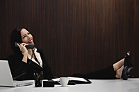 A woman talks on the phone while she is at her desk - Asia Images Group