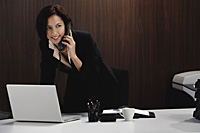 A woman talks on the phone while she is at her desk - Asia Images Group