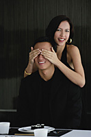 A woman covers her boyfriends eyes as she prepares to surprise him with dinner - Asia Images Group