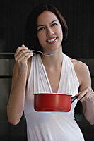 A woman tastes her cooking as she looks at the camera - Asia Images Group