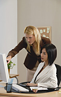 Two woman look at a computer while at work - Asia Images Group