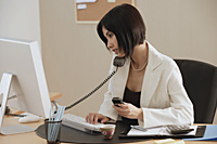 A woman talks on the phone while she is at work - Asia Images Group