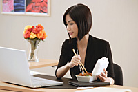 A woman eats lunch at her desk while she works - Asia Images Group