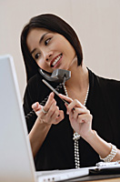 A woman files her nails as she talks on the phone at work - Asia Images Group