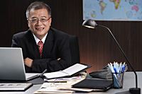 A man smiles at the camera as he sits at his desk - Asia Images Group