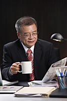 A man having a drink while working at his desk - Asia Images Group