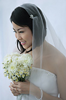 A bride smiles as she holds a bouquet of flowers - Asia Images Group