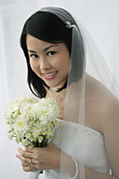 A bride with a bouquet of flowers looks at the camera - Asia Images Group
